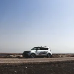 Kia Soul in a used-car lot with a buyer and mechanic inspecting it in natural light