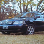 Volvo XC90 parked on a driveway with a mechanic inspecting the front wheel and open hood